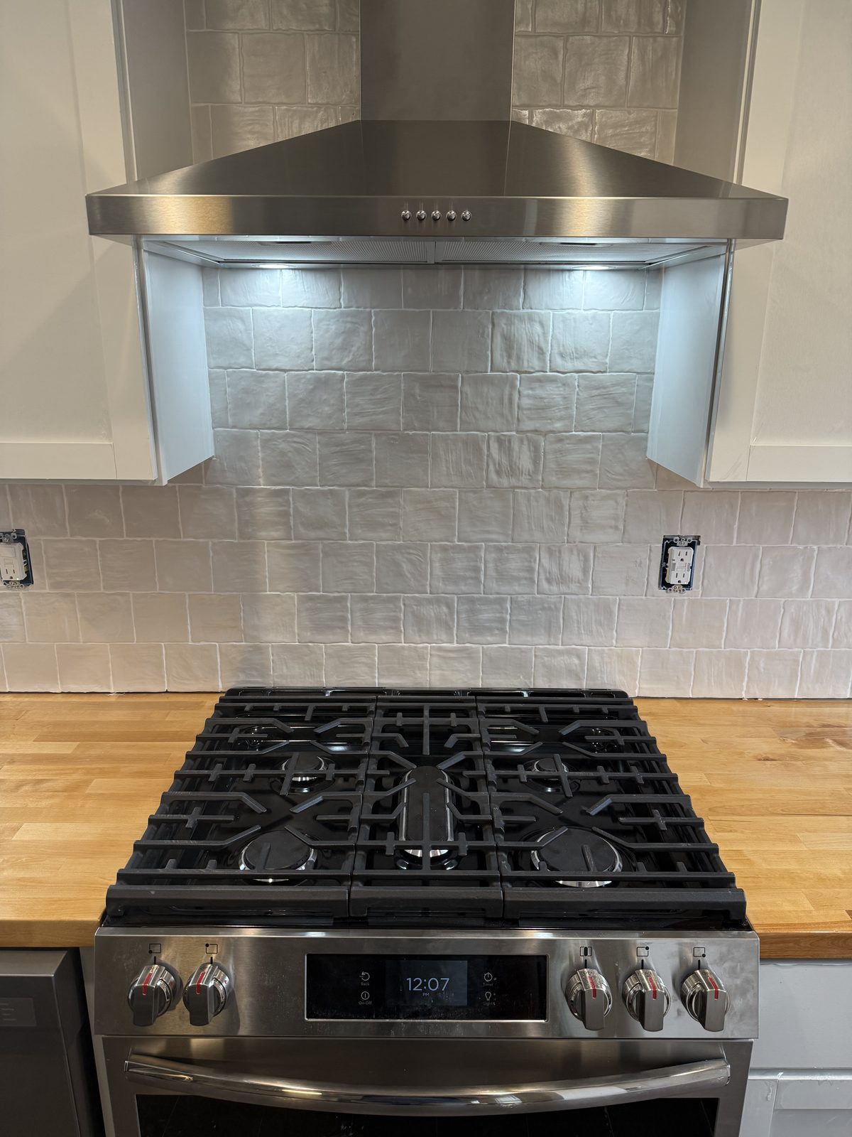 Kitchen remodel with a stainless range hood over handmade tile backsplash